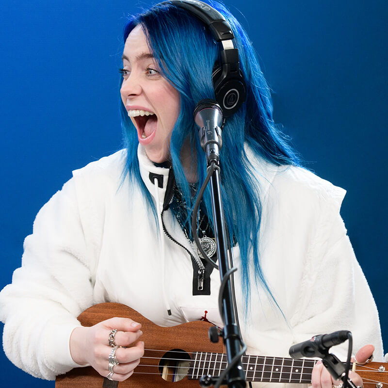 Billie Eilish laughing while playing a Ukulele.