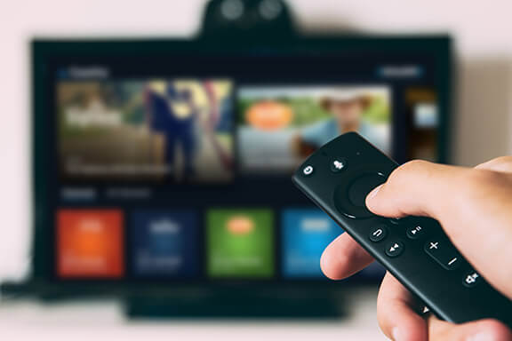 A man pointing a Amazon FireTV remote at a television.
