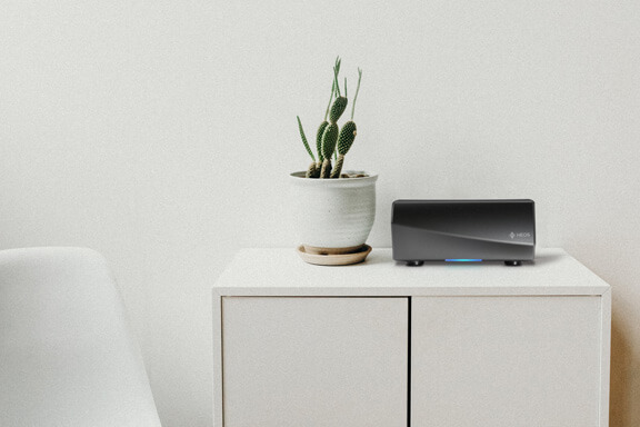 Un haut-parleur HEOS à côté d’une plante sur une étagère.