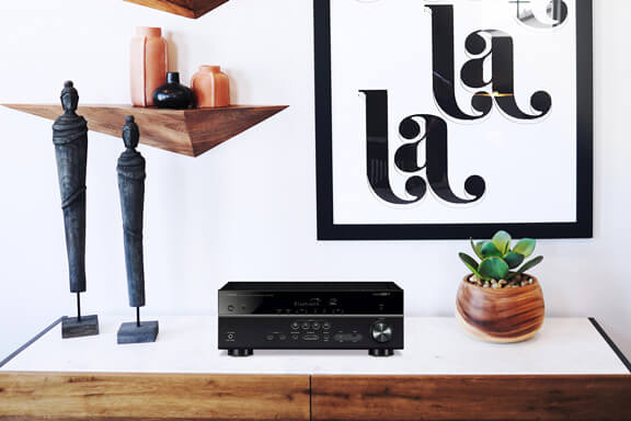 A Yamaha receiver on a shelf beside two statues and a plant.