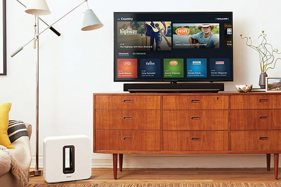 A television displaying the SiriusXM App with a Sonos Soundbar underneath it.