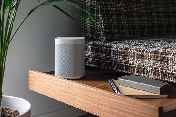 A Sonos speaker located on a side table beside a couch.