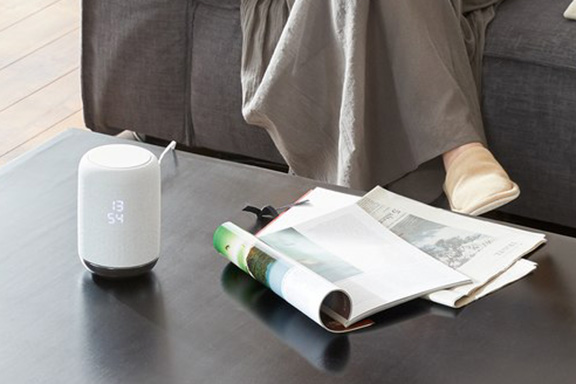 A speaker on a coffee table surrounded by magazines and newspapers.