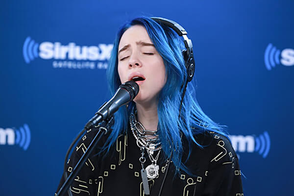 An image of Billie Eilish singing with her eyes closed.