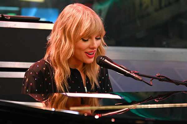 An image of Taylor Swift sitting behind a piano.