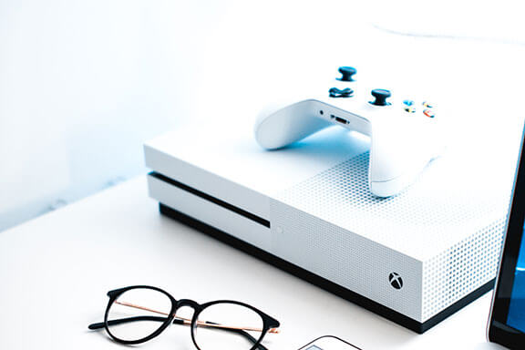 A white Microsoft Xbox One and controller beside a pair of glasses.