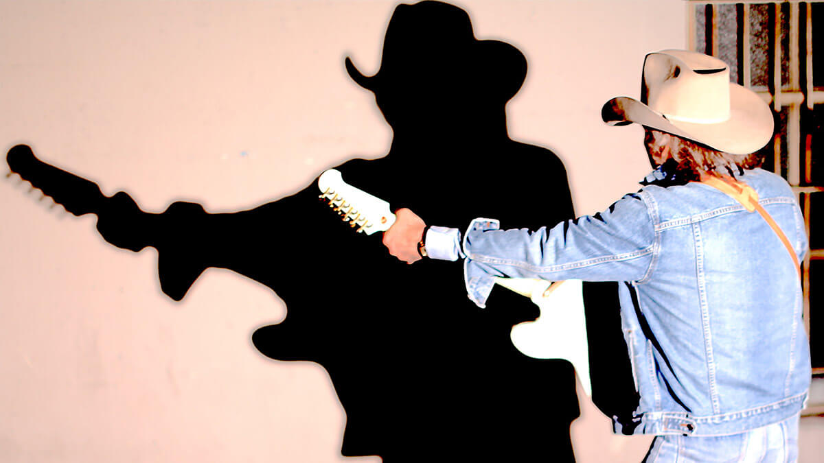 An image of Dwight Yoakam with his back turned to the camera and facing his shadow.