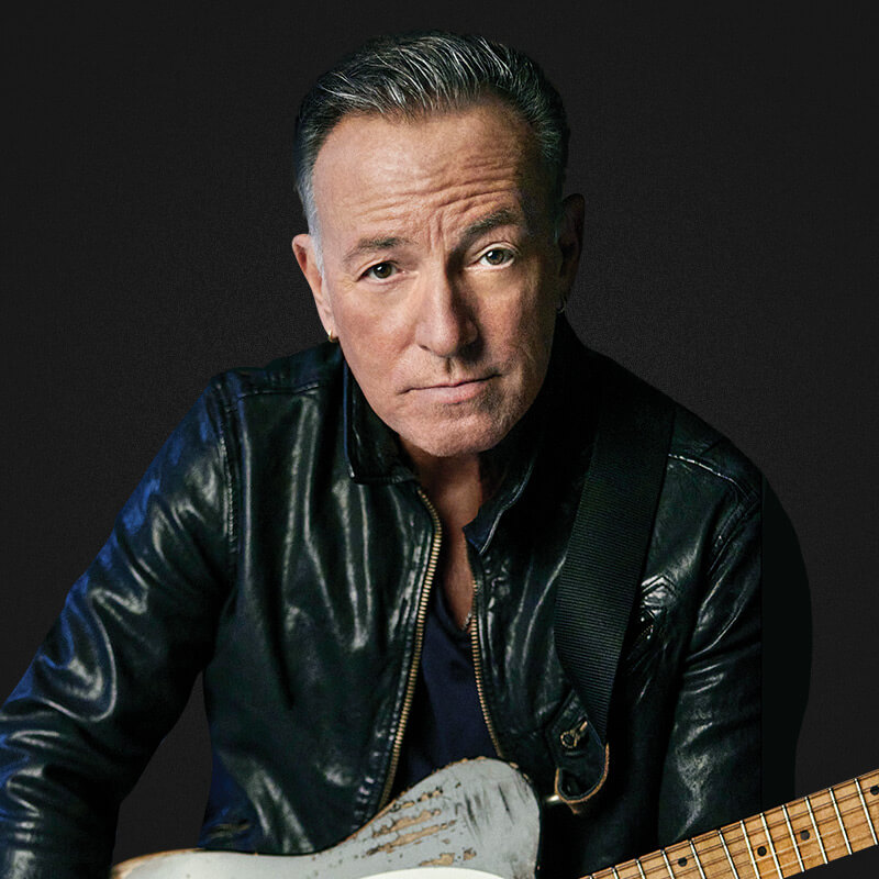Bruce Springsteen in a black leather jacket holding his guitar.