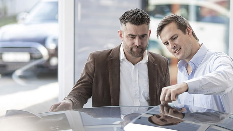 Two men inspecting the sunroof of a new car at a dealership.