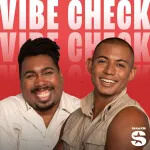 Two smiling men pose in front of a red background with the large white text VIBE CHECK behind them. One man has short hair and a beard, and the other has very short hair and wears a sleeveless shirt—Listen to the Vibe Check podcast on SiriusXM.