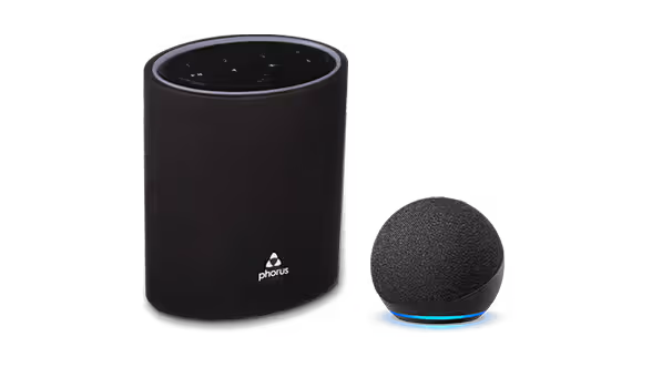 A black cylindrical Phorus speaker sits next to a small, spherical black Amazon Echo Dot smart speaker with a glowing blue ring near its base.
