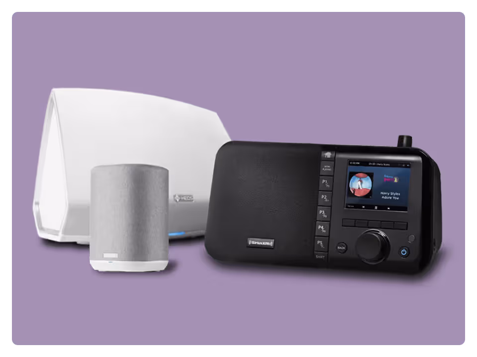 Three music devices on a purple background: a white HEOS wireless speaker, a smaller silver speaker, and a black SiriusXM Soundstation radio displaying music playback information.