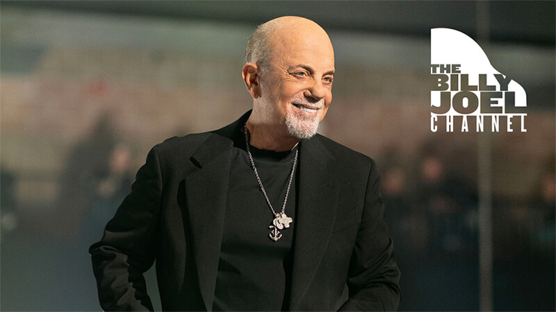 Billy Joel is pictured with a grey goatee wears a black jacket and necklace. The Billy Joel Channel logo is displayed in the background. Listen to The Billy Joel Channel exclusively on SiriusXM.